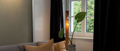 Una sala de estar moderna con un sofá gris, una mesa de centro de madera y una ventana con cortinas negras.