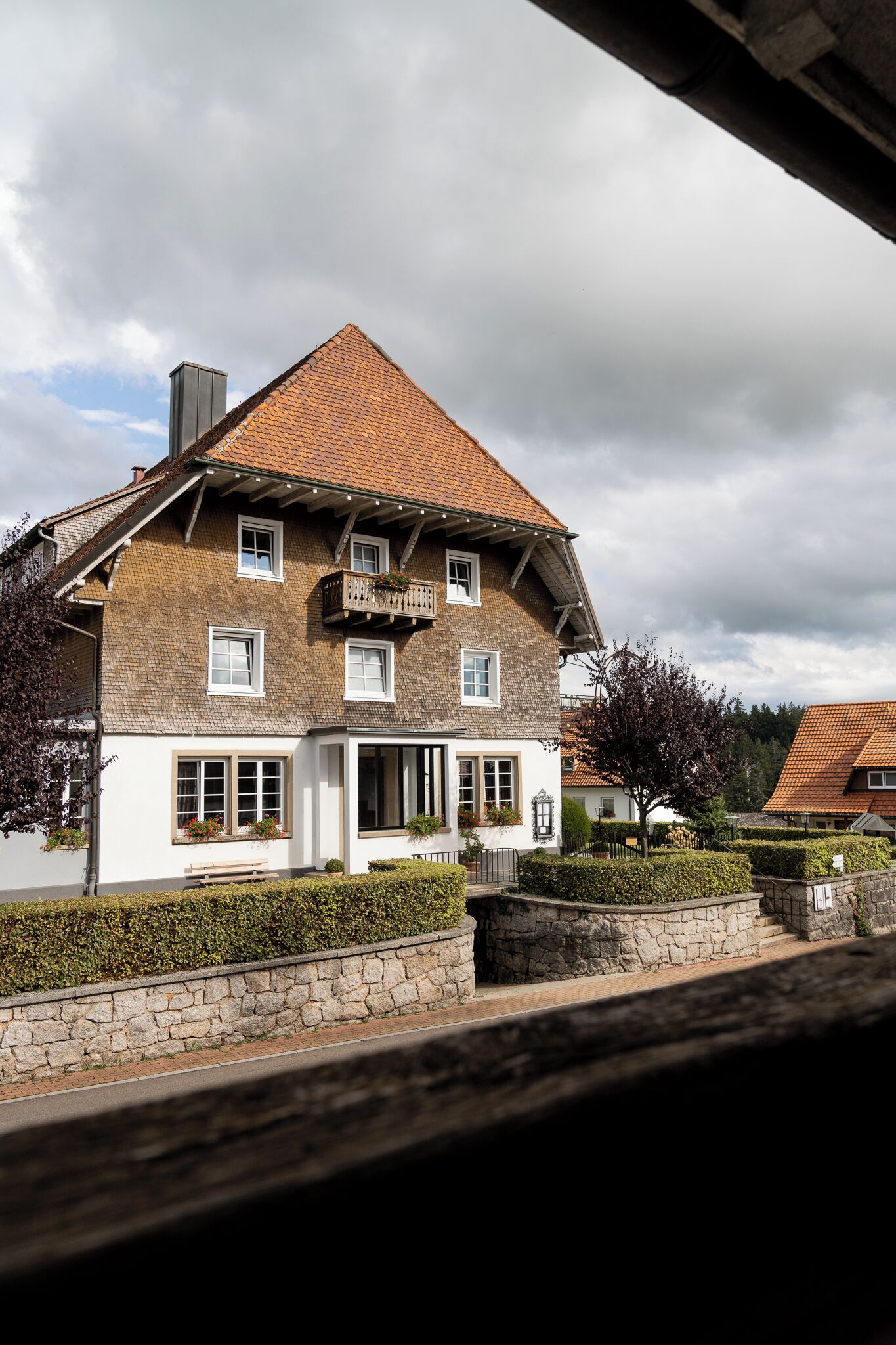 Ein zweistöckiges Haus mit einem geneigten Dach, einem mit Pflanzen bepflanzten Balkon und einem Steinweg, der zum Eingang führt.