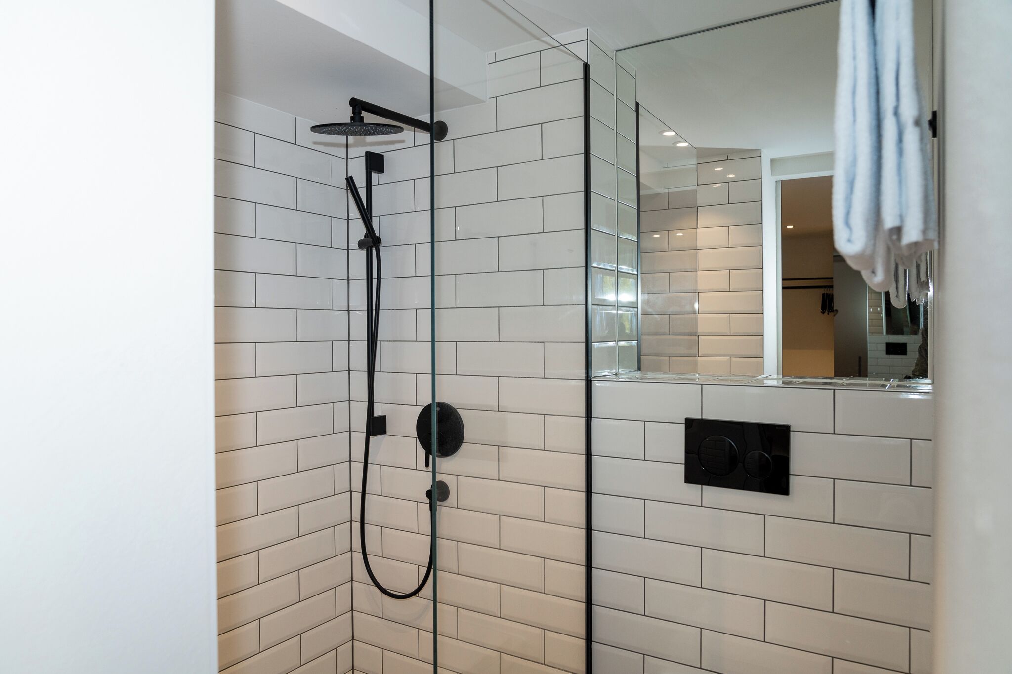 A modern bathroom with white tiled walls, a glass shower enclosure, and a visible towel rack.