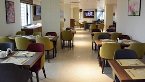 A hotel dining area with multiple tables and chairs, a television screen, and artwork on the walls. - Capital Hotel Djibouti (Djibouti)