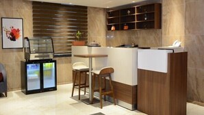 A modern kitchen with a wooden counter, two bar stools, a refrigerator, and a decorative plant. - Capital Hotel Djibouti (Djibouti)