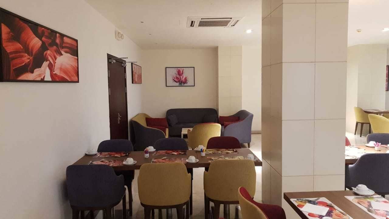 Een eetruimte met een tafel gedekt voor vier personen, omringd door stoelen. Er hangen ingelijste foto’s aan de muur.