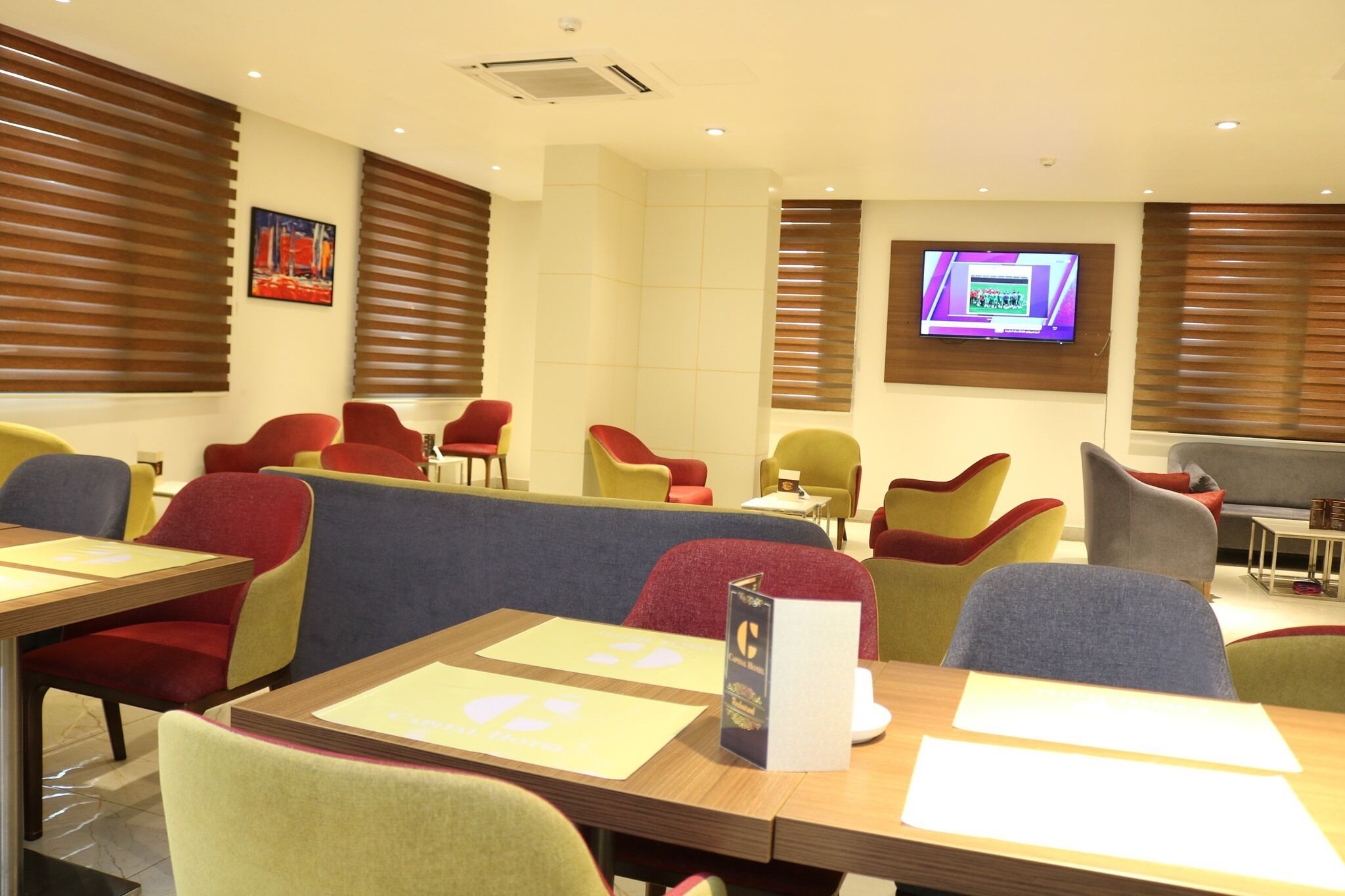 A modern dining area with booths and chairs, a flat-screen TV on the wall, and a menu stand.