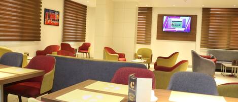 A modern dining area with booths and chairs, a flat-screen TV on the wall, and a menu stand.