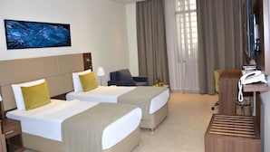 A hotel room with two beds, a desk, a TV, and a large window with curtains. - Capital Hotel Djibouti (Djibouti)