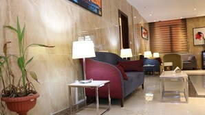 A modern hotel lobby with a marble wall, a potted plant, a sofa, two side tables with lamps, and a small table with a cup. - Capital Hotel Djibouti (Djibouti)