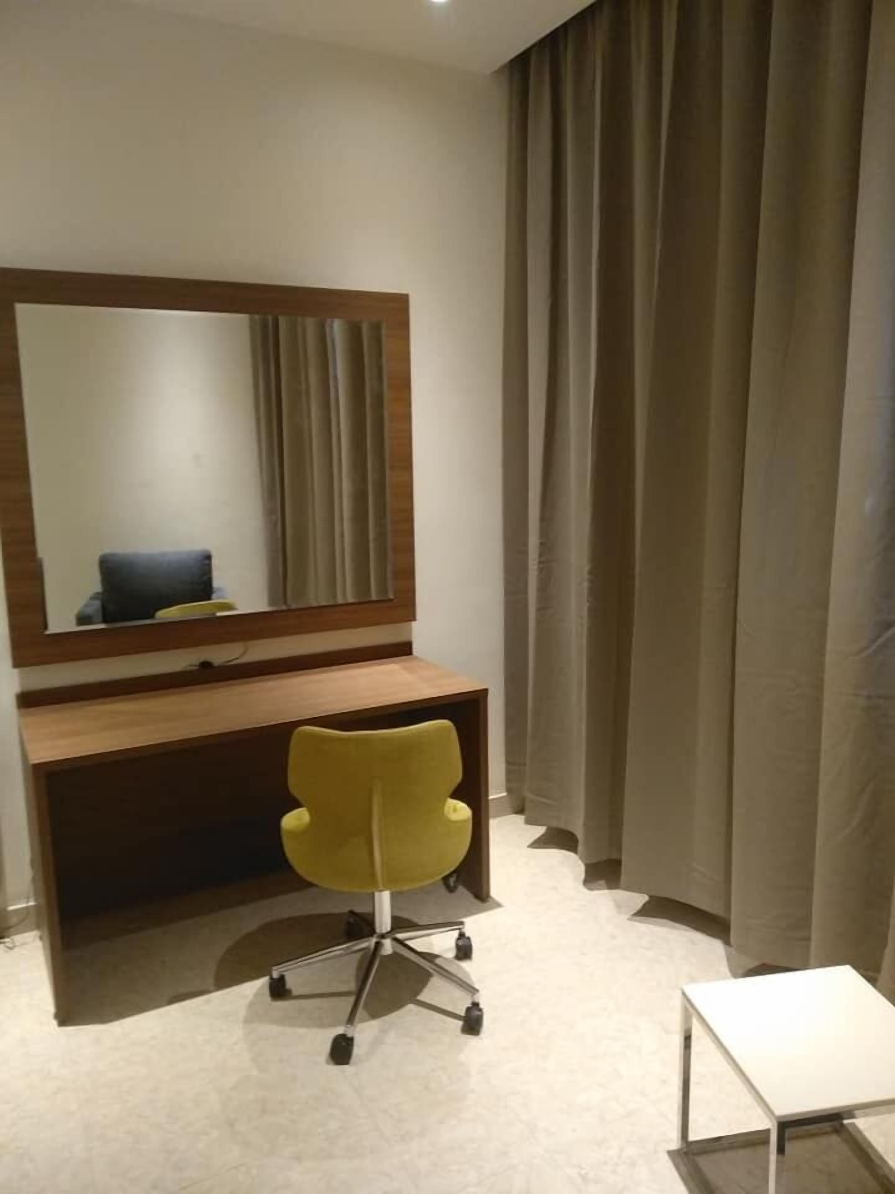 Una habitación de hotel moderna con un escritorio de madera, una silla de oficina amarilla, una mesita blanca peque ña y un espejo grande.