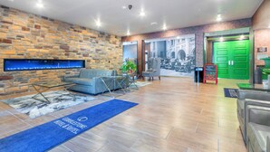 A hotel lobby with a stone wall, a sofa, a coffee table, a reception desk, and a green door. - Cobblestone Hotel and Suites Janesville (Janesville)