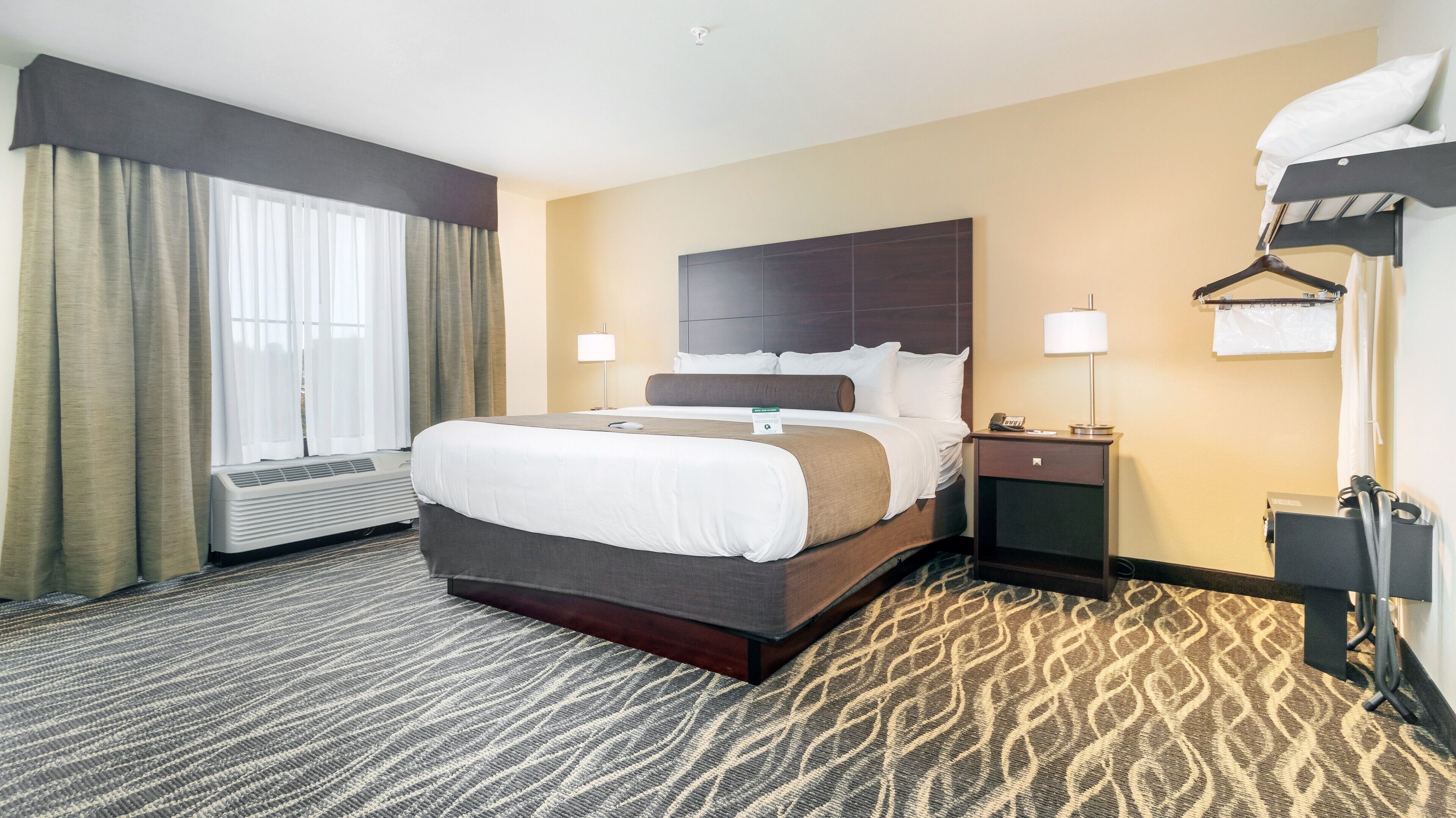 Quarto de hotel com uma cama grande, mesas de cabeceira, aquecedor, abajur e cabideiro.