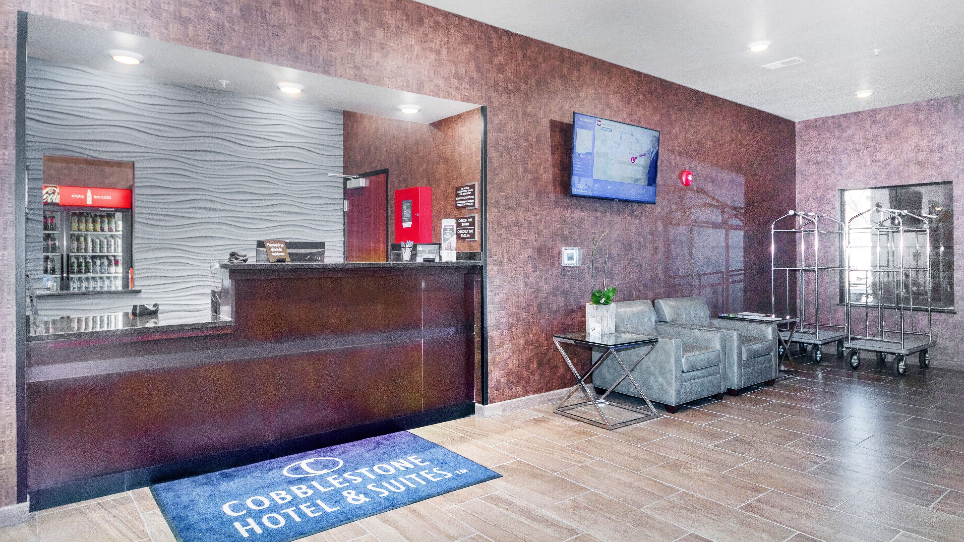A hotel reception area with a modern design, including a reception desk, seating area, and a television mounted on the wall.