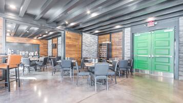 A modern dining area with tables and chairs, a green exit door, and a stone wall.