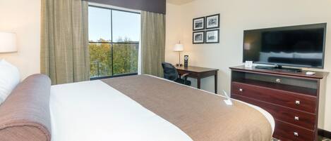 Quarto de hotel com uma cama grande, uma escrivaninha com cadeira, televisão e janela com cortinas.