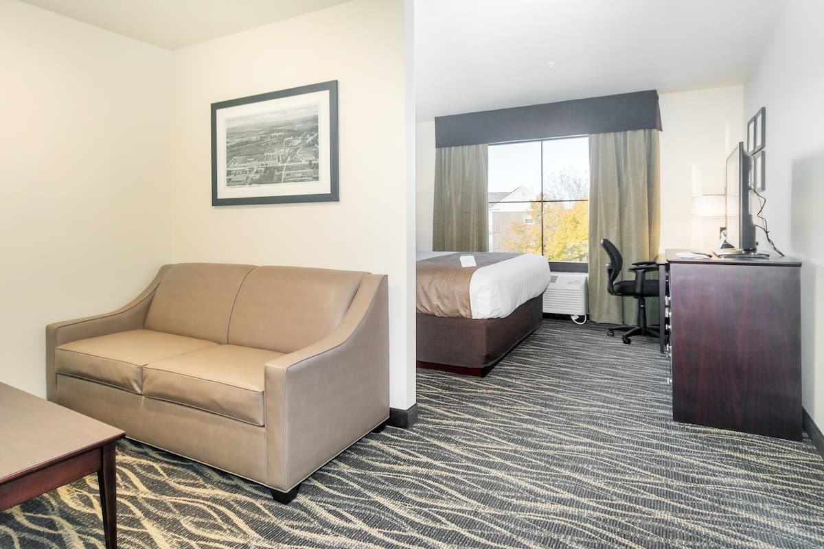 Ein Hotelzimmer mit einer Couch, einem kleinen Tisch mit Fernbedienung, einem Bett, einem Schreibtisch und einem gerahmten Bild an der Wand.