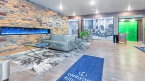 A lobby with a stone wall, a sofa, a glass coffee table, a fireplace, and a green door. - Cobblestone Hotel and Suites Janesville (Janesville)