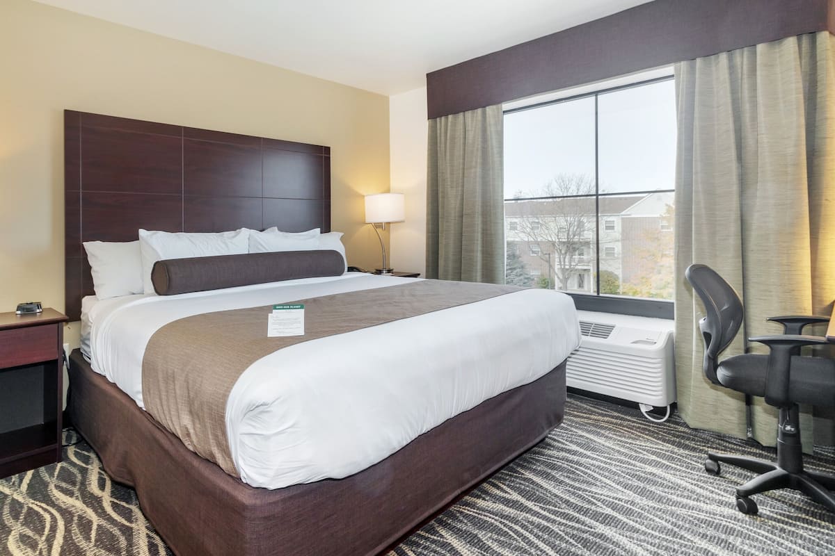 Ein Hotelzimmer mit einem großen Bett, zwei Nachttischlampen, einem Schreibtisch mit Stuhl und einem fenster mit Vorhängen.