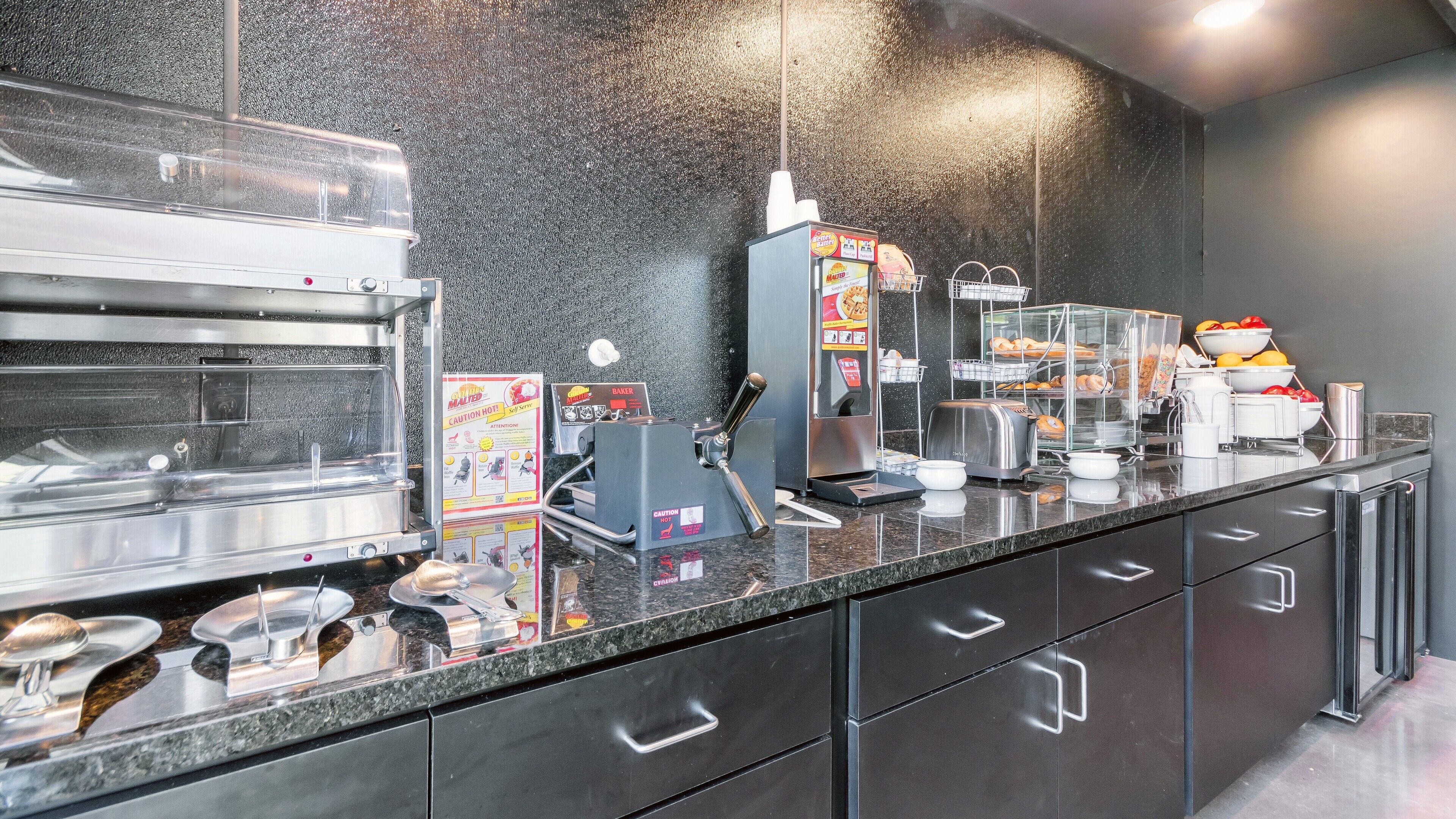 A buffet setup with a self-service food station, a coffee machine, and a variety of food items displayed in clear containers.