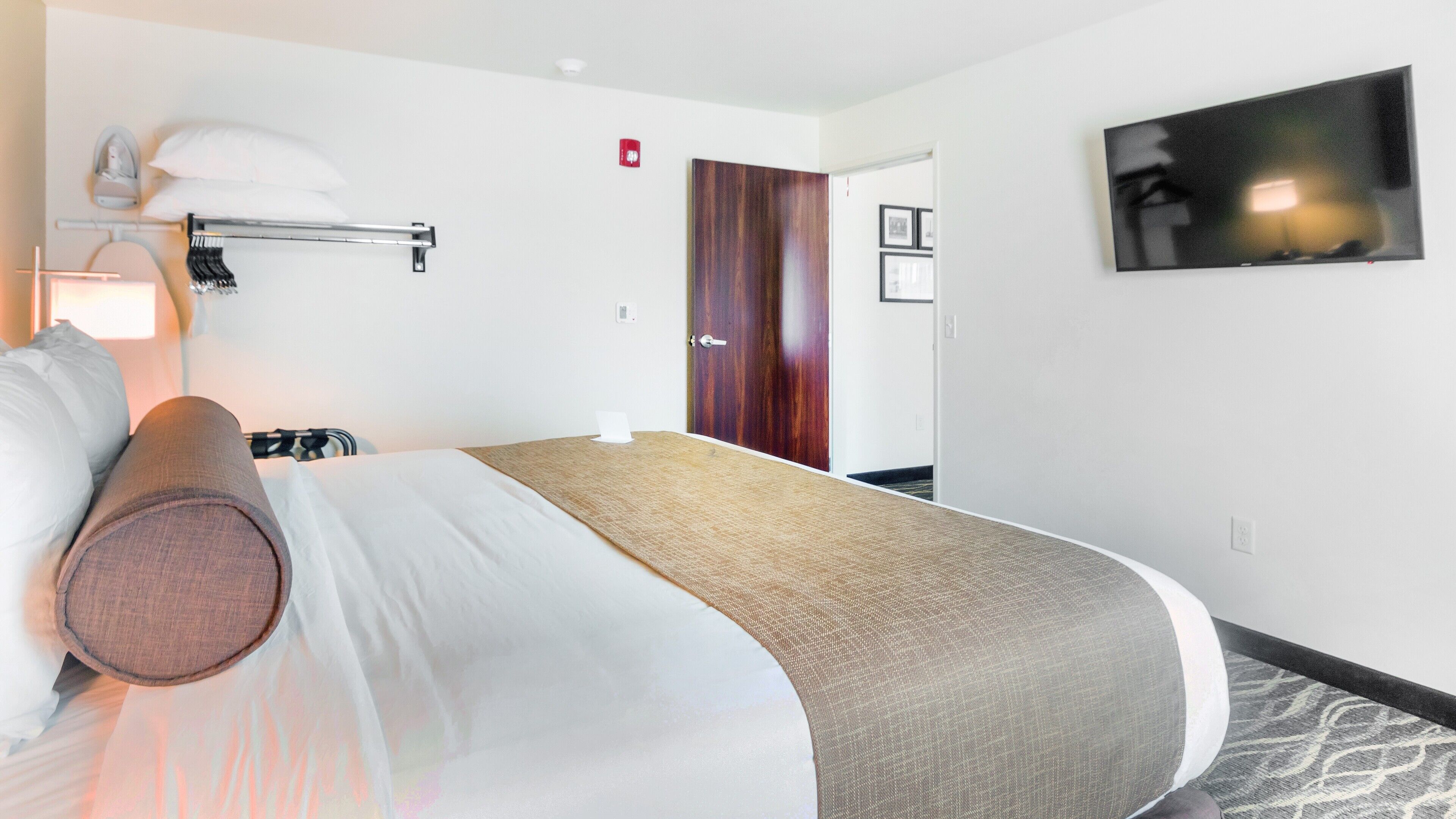 A hotel room with a bed, a flat-screen TV, a door, and a hallway.