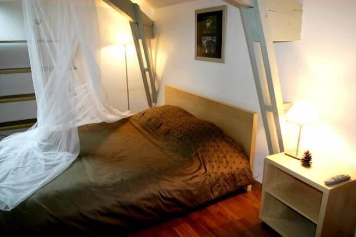 Een slaapkamer met een bed, nachtkastje, lamp en een foto aan de muur.