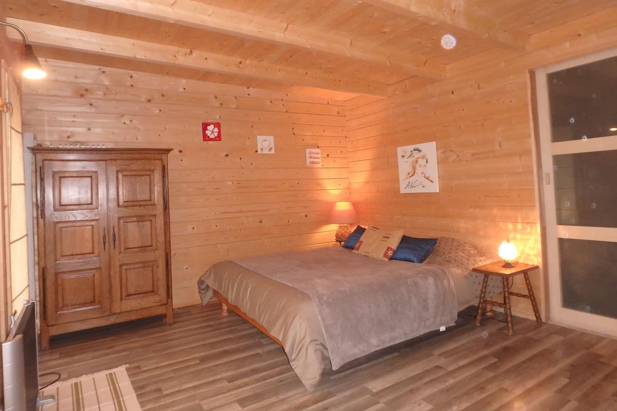 Een kamer met houten lambrisering, een bed, een houten kledingkast, een lamp en een raam.