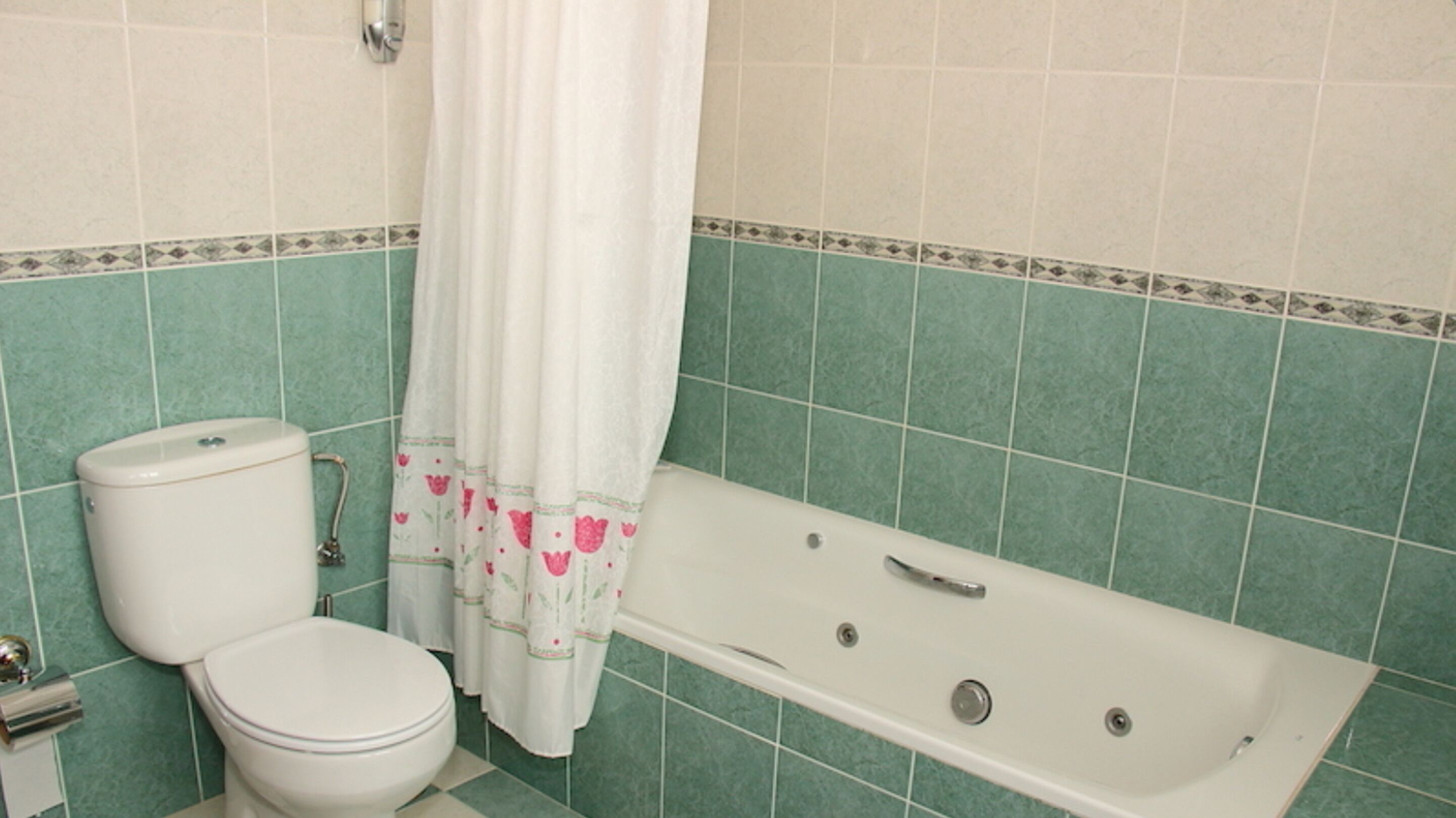 A bathroom with a toilet, bathtub, and green tiled walls.