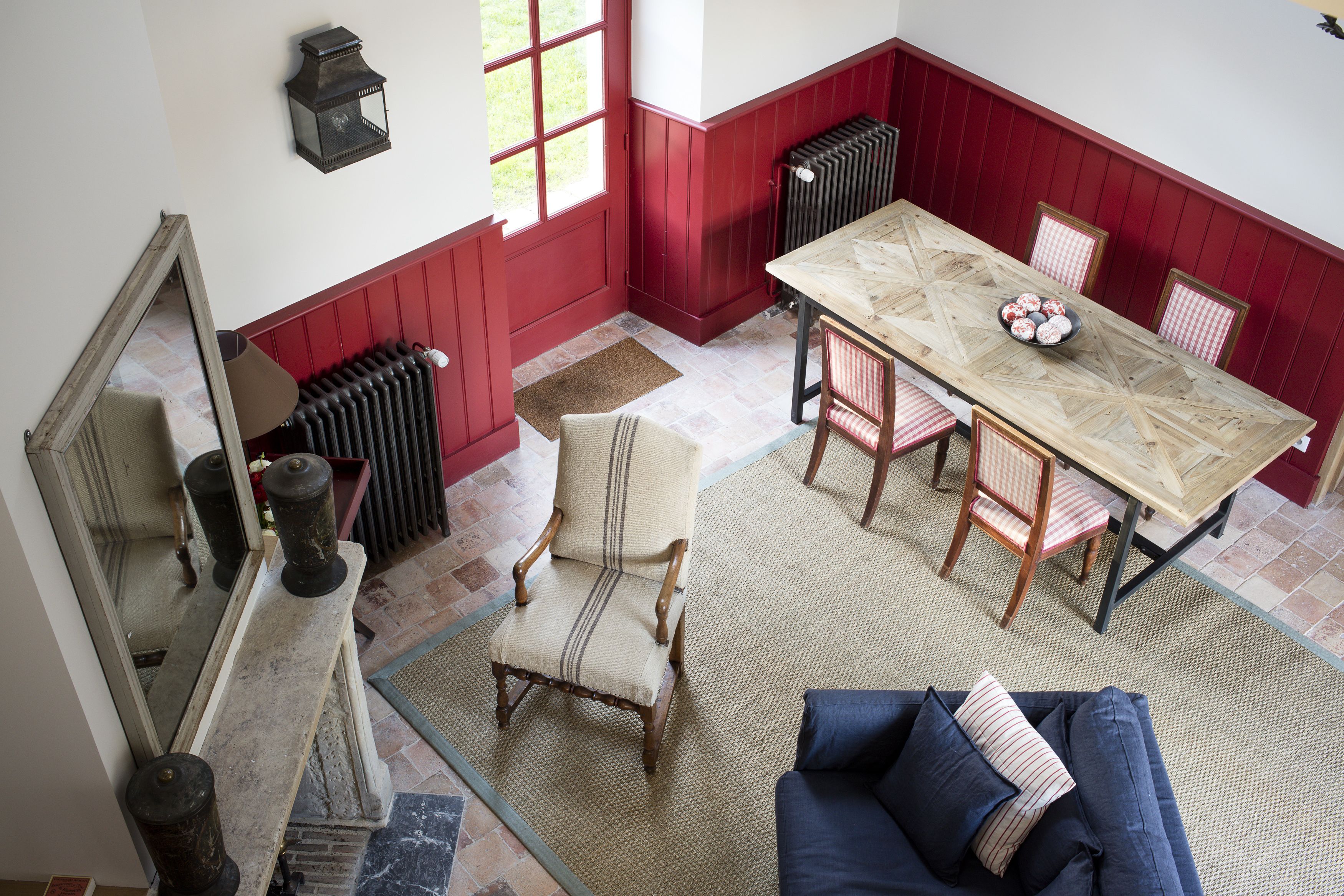A dining area with a wooden table, red paneled walls, and a blue sofa.