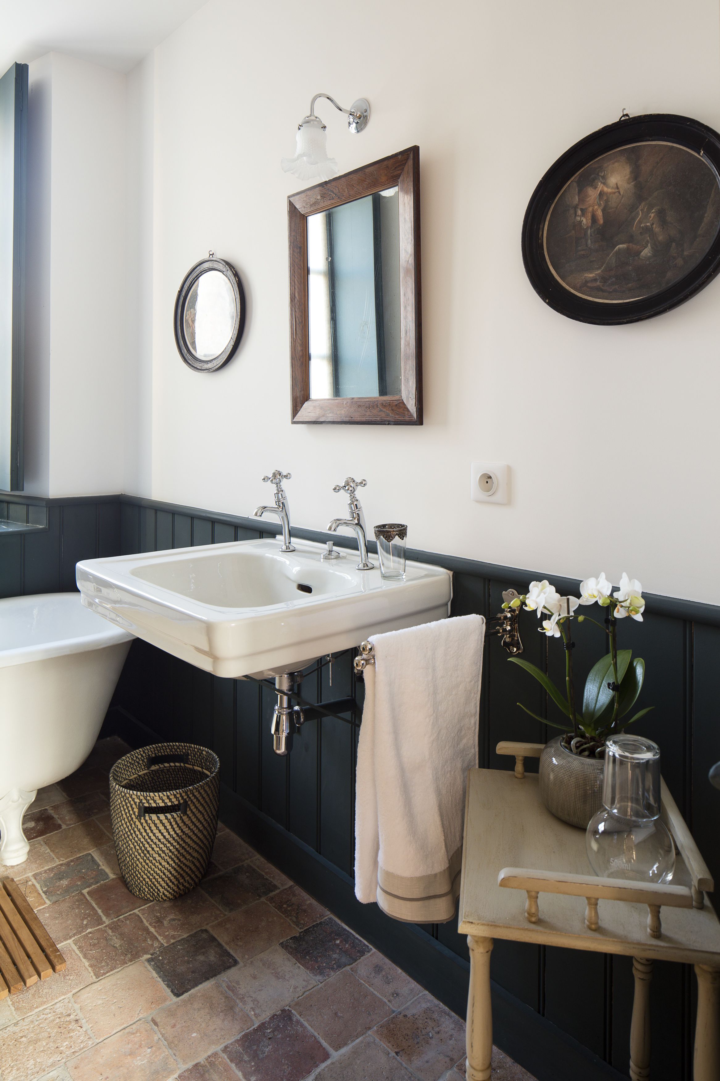 A bathroom with a white bathtub, a sink, and a mirror. There is a towel hanging on the wall and a small table with a vase of flowers.