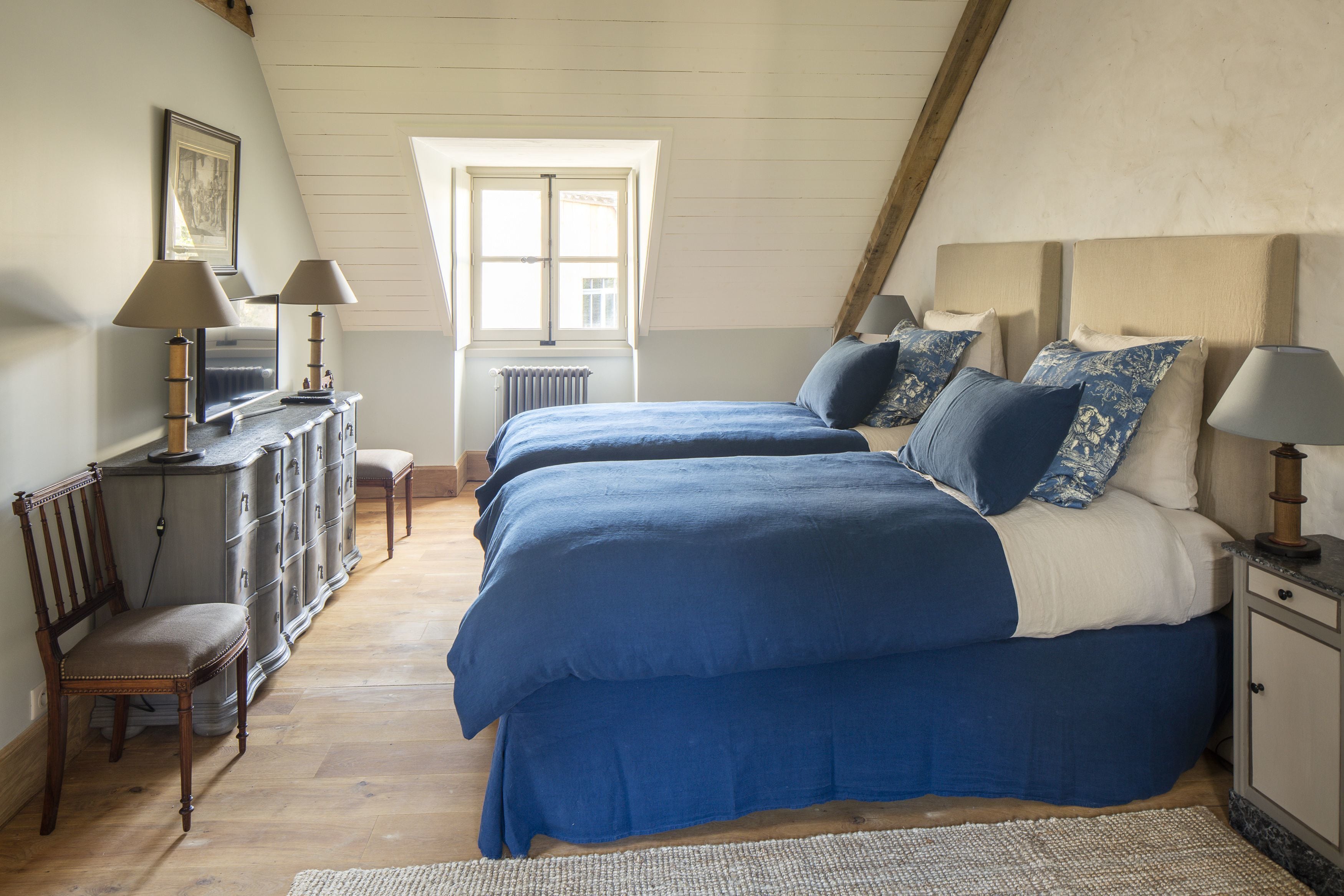 Ein Schlafzimmer mit zwei Betten, einem Schminktisch, einem Sessel und einem Fenster.