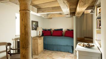 Una camera da letto con soffitto in legno, un letto con biancheria rossa e blu, un comodino con una lampada e una sedia.