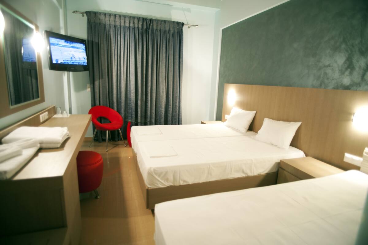 A hotel room with two beds, a TV, a desk, and a red chair.