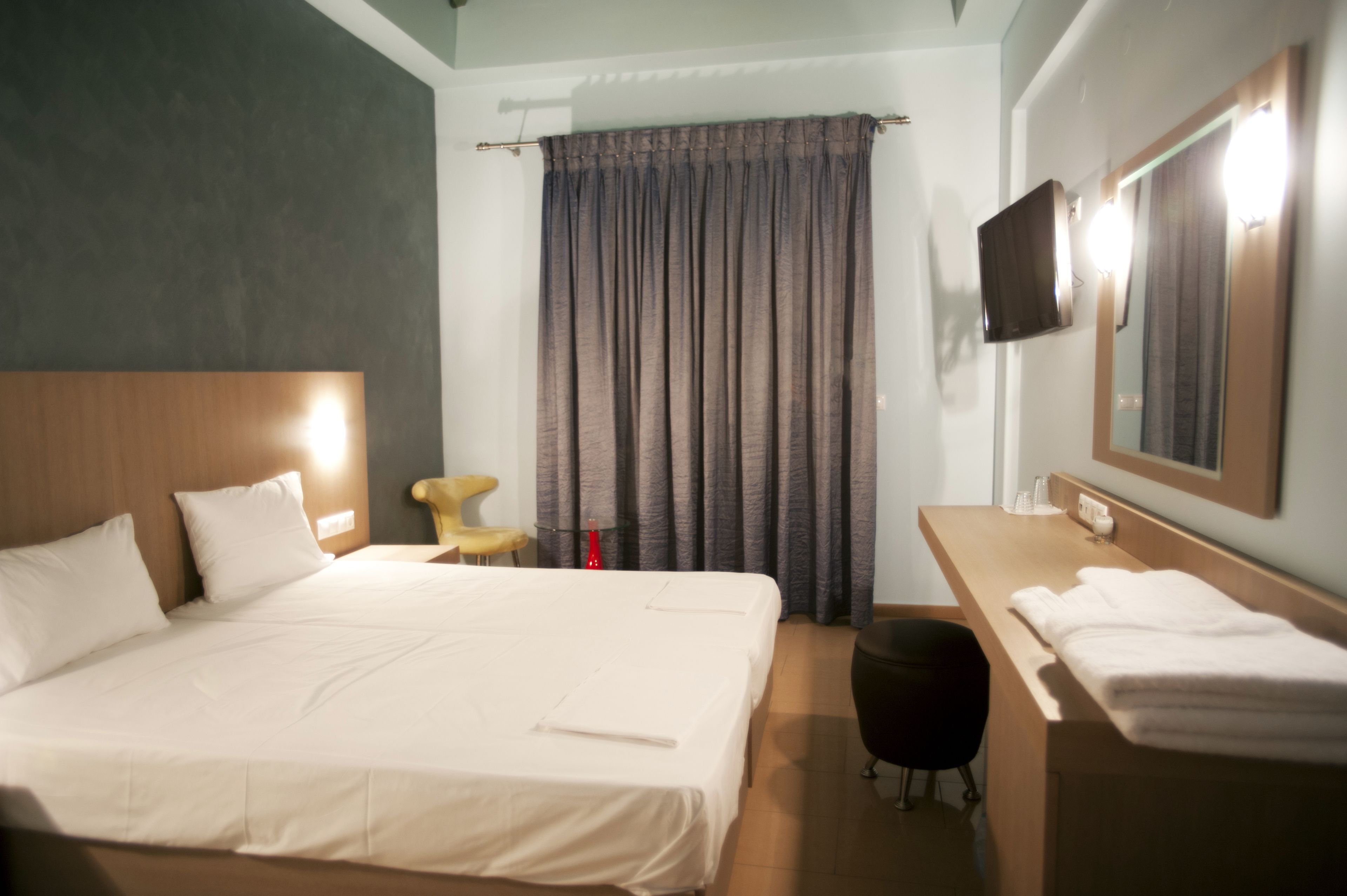 A hotel room with a large bed, a bedside table with a lamp, a TV mounted on the wall, and a bathroom with a mirror and towel rack.