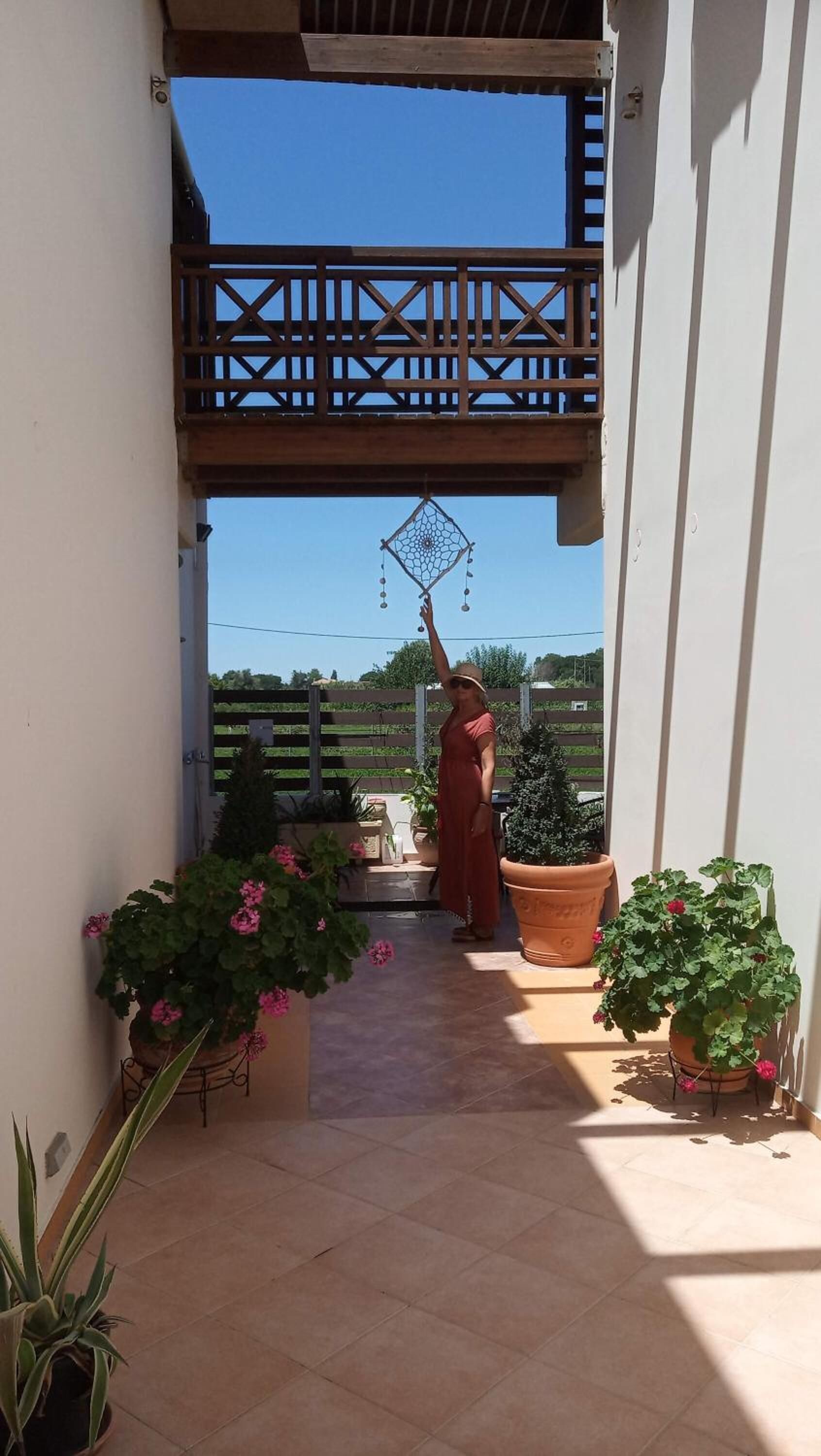 A covered outdoor area with a wooden railing, potted plants, and a person holding a decorative item.