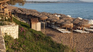 A beach with thatched umbrellas and sun loungers, a stone wall, and a view of the sea. - Giovanni Mare (Ilida)