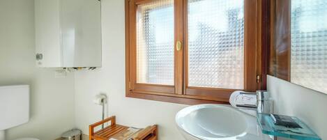 A bathroom with a toilet, sink, and window.
