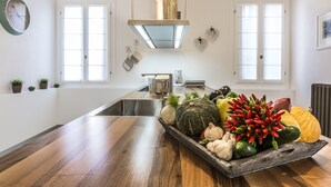 Une cuisine moderne dotée d’un plan de travail en bois, d’un îlot central où sont présentés des fruits et des légumes, d’un évier en acier inoxydable et d’un luminaire suspendu.