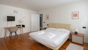 Ein Schlafzimmer mit Bett, Schreibtisch, Stuhl, Fernseher und Nachttisch mit Lampe.