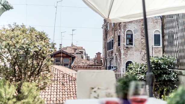 A terrace with a table and chairs, overlooking a street with buildings and a tree. - Three Terraces (Venice)