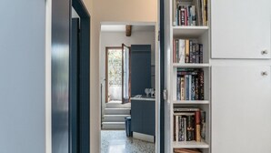 A hallway with a staircase leading to a kitchen area, a bookshelf filled with books, and a door leading to another room. - Three Terraces (Venice)