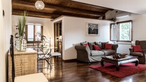 A living room with a wooden ceiling, a sofa set, a coffee table, and a dining area with a metal chair and table.