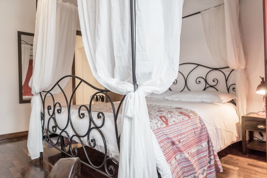 Uma cama de dossel com dossel branco, um edredom estampado e uma mesa de cabeceira com abajur.