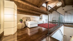 A spacious loft bedroom with a wooden ceiling, a white sofa, a red rug, and a staircase with metal railings.