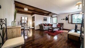 A spacious living room with wooden flooring, a dining area with a table and chairs, and a cozy seating area with a sofa and armchairs.