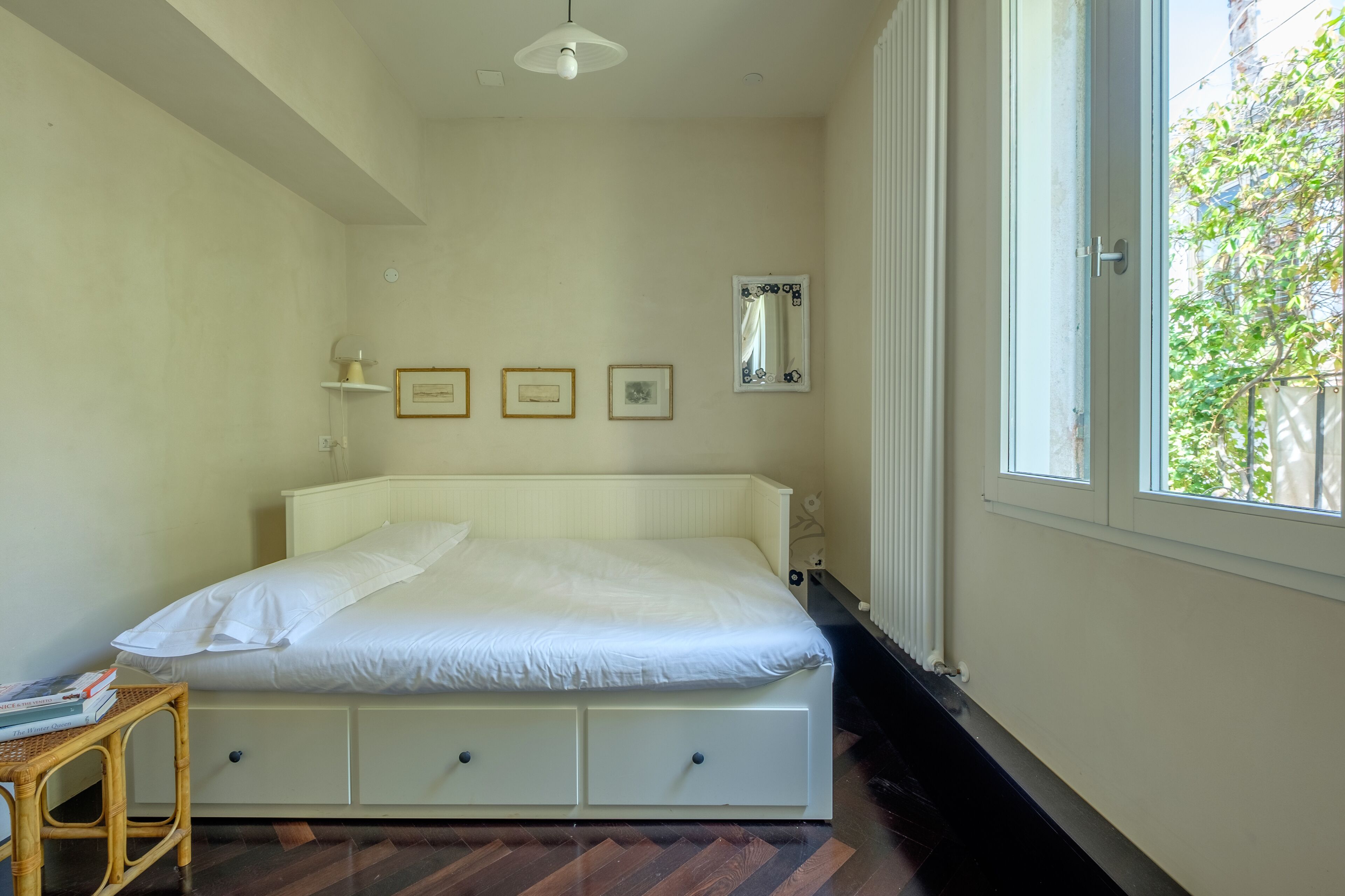 A bedroom with a bed, a bedside table, a mirror, and a window.