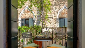 A cozy outdoor seating area with two orange cushioned chairs and a small table, set against a rustic brick wall with a tree and greenery. - Attico Terrazza (Venice)