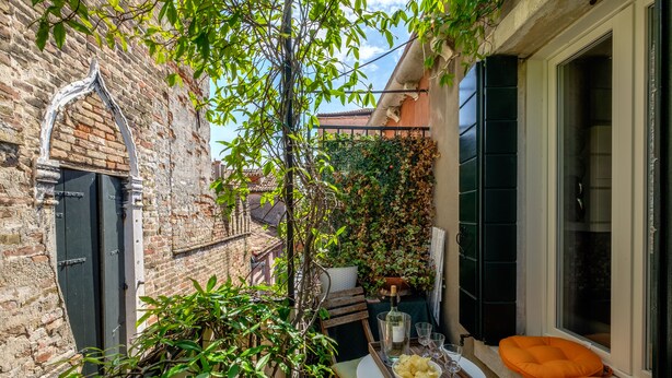 A small patio with a table set for two, a chair, and a window with a view of the city. - Attico Terrazza (Venice)