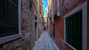 A narrow alleyway with stone pavement, brick walls, and a mix of open and closed windows. - Attico Terrazza (Venice)
