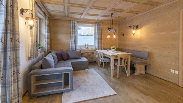 Um quarto aconchegante com sofá seccional, mesa de jantar com cadeiras, um banco e janela com cortinas.