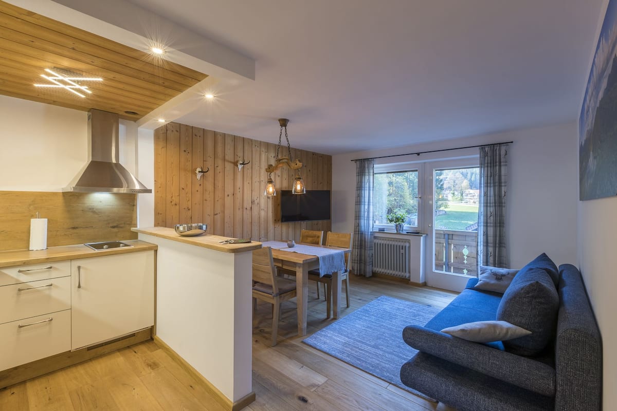 A modern kitchen with wooden accents, a dining area with a table and chairs, and a cozy living room with a sofa.