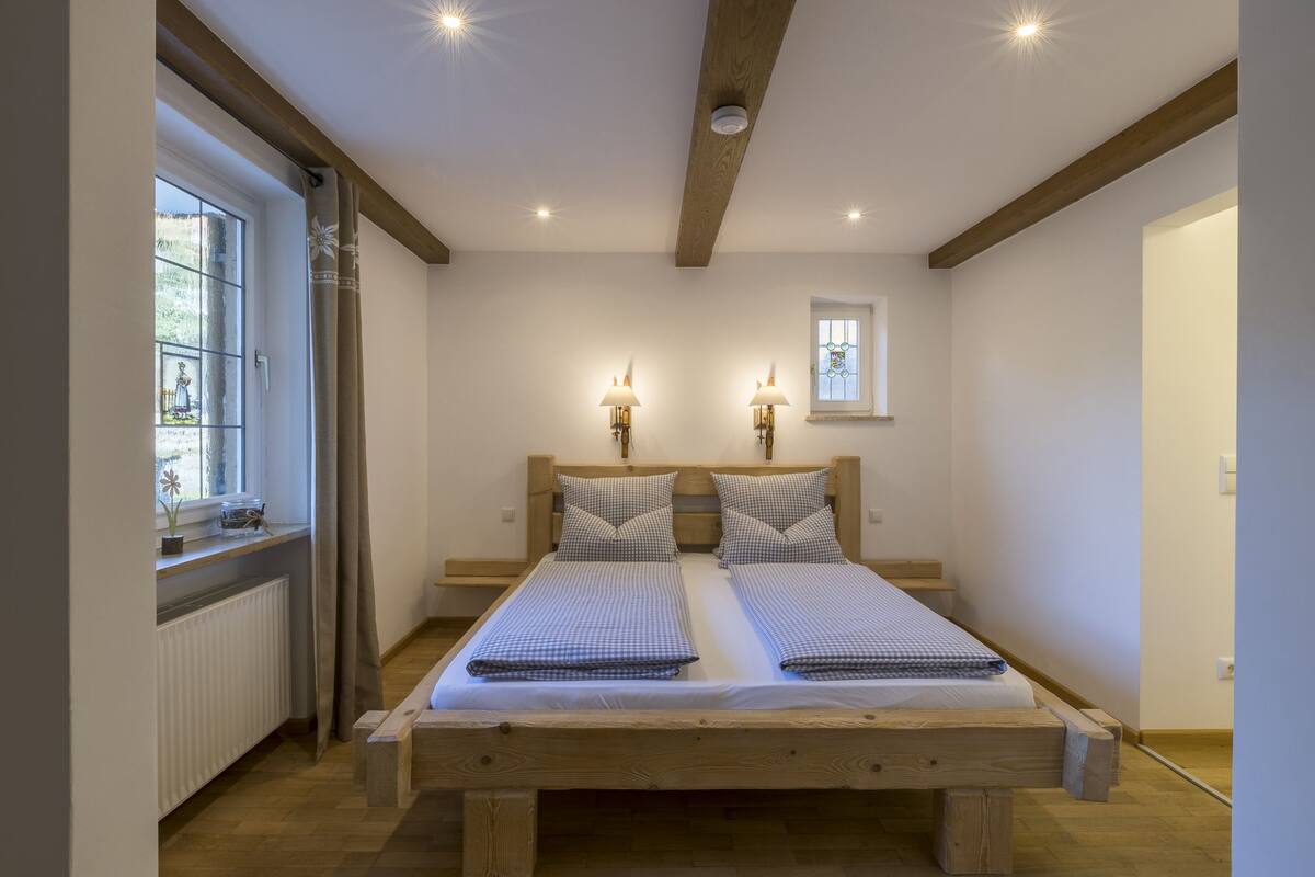 A double bed with a wooden frame, two bedside lamps, a window with a view, and a radiator.