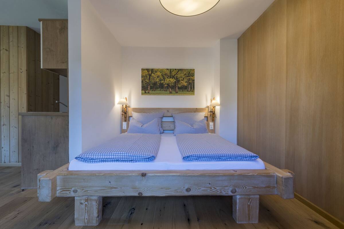 A bedroom with a wooden bed frame, two bedside tables with lamps, a painting on the wall, and a wooden wardrobe.
