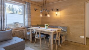Um quarto aconchegante com teto de madeira, uma mesa de jantar com cadeiras, um banco, um sofá e uma janela com cortinas.